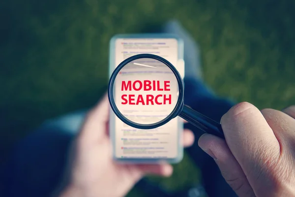 Top-down view of a sitting man with the magnifying glass with written red words Mobile Search above the smartphone screen. Man uses cell phone to browse search engine. Concept of mobile searching