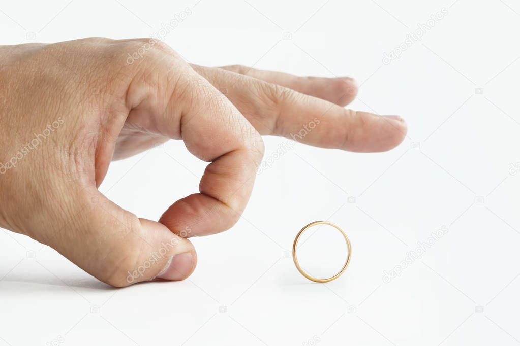 Close up of person's hand pushing away wedding golden ring isolated on white. Man makes finger kick of a ring. Male unwilligness to stay married. Disillusionment in marriage. Divorce initiated by men