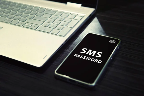 Table with open laptop and black-screened smartphone with white written words SMS password on its display. Concept of linking the work of computer and mobile via sms password entering. One time code. — Stock Photo, Image