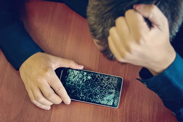 Desperate and astonished man holds cracked smartphone . Screen broken smartphone. Cracked phone Broken phone. Sad guy holding a broken expensive smartphone