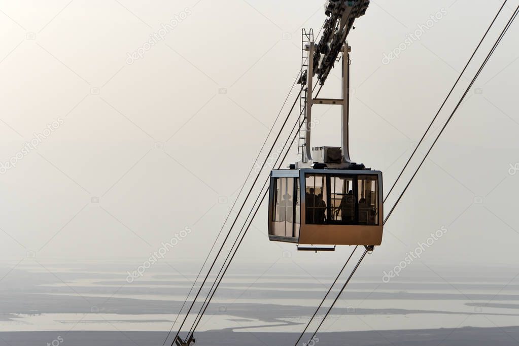 cable car lifts tourists to the mountain fortress of Masada. Funicular on the background of the Judean desert, the dead sea and the cloudy sky. Desert beautiful landscape.
