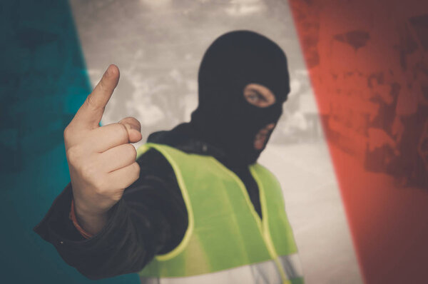 Yellow vests protest against higher fuel prices in France. concept of street protests of workers, proletarians against system, bourgeoisie. man in a mask and a yellow vest on background of French flag