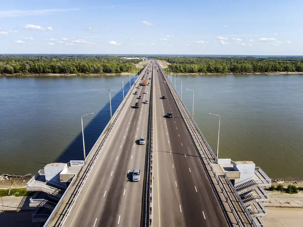 A view to the well-built city bridge across the river. City river gates. Trasportation across the river at the forest and horizon background. Vehicular traffic on the highway across the river