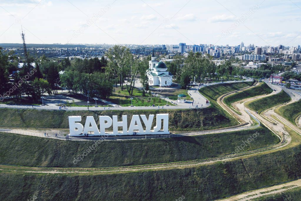 A picturesque bird's eye view to the letters on the slope spelling out a Russian city's name. The developed touristic area with the monumental city name construction on the stepwise green hill.