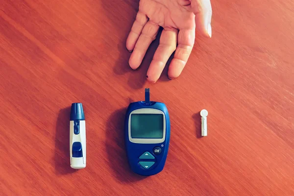a lady\'s hands measuring blood sugar, glucose with a home test to control her diabetes. Blood glucose meter and needles for the test lie on a wooden table. drop of blood on finger close up