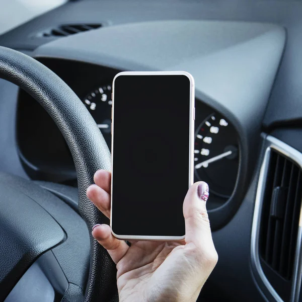 Close up of woman's hand holding mobile phone with black screen while driving a car. Female using smart phone sitting in driver seat. Girl stops the car to check her phone. Steering wheel and gadget