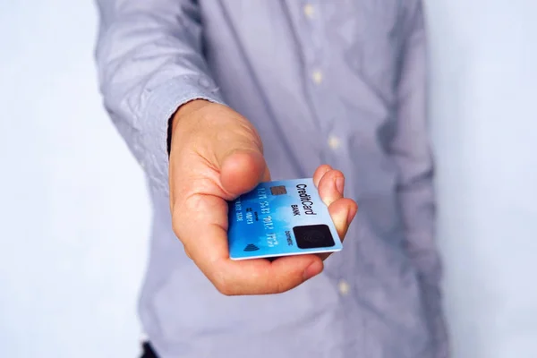 Casual young businessman at blue background giving credit card with fingerprint scanner on its front side. Close up shot focused on the male hand holding the payment card with biometric scanner