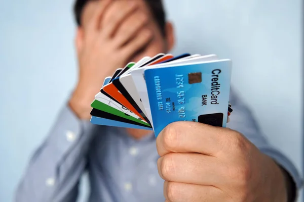 Hombre confundido mirando muchas tarjetas de crédito incierta cuál elegir en el fondo azul. joven está sosteniendo una parada de tarjetas de crédito y débito en una pose pensativa. El tipo elige una tarjeta para pagar — Foto de Stock