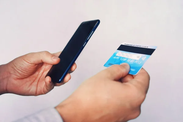 Conceito de pagamento online. Homem usando cartão de crédito com telefone celular em fundo branco. Mãos masculinas segurando smartphone com tela em branco e cartão de banco reverso. A pessoa paga usando celular. Transação . — Fotografia de Stock