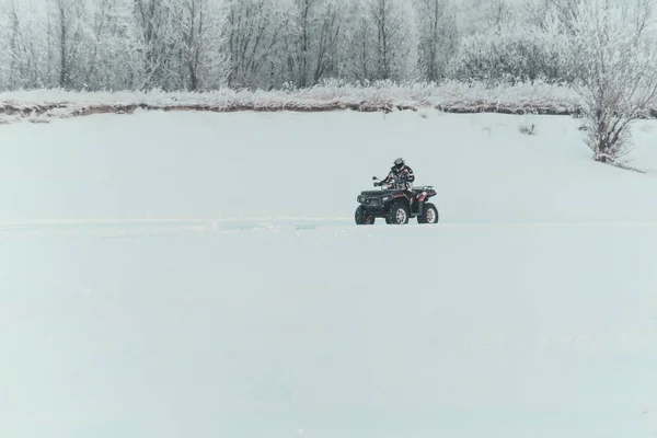 Unidentified motocross rider on quad bike at Opening motocross season race. winter motocross. ATVs are riding in the field in the snow on the background of snowy trees