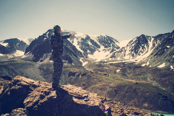 Chico admira el hermoso paisaje de montaña. El hombre está de pie en el acantilado, contra el telón de fondo del lago y las montañas. Concepto de viaje, pesca, turismo en Rusia — Foto de Stock