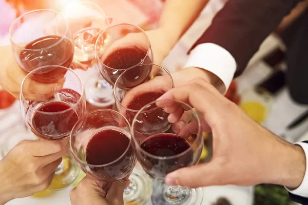 Male and female hands with filled glasses of wine above the restaurant tabletop. Drinking toasts and clinking tumblers at a formal dinner party. Drinking wine at a banquet. In full swing of a feast.