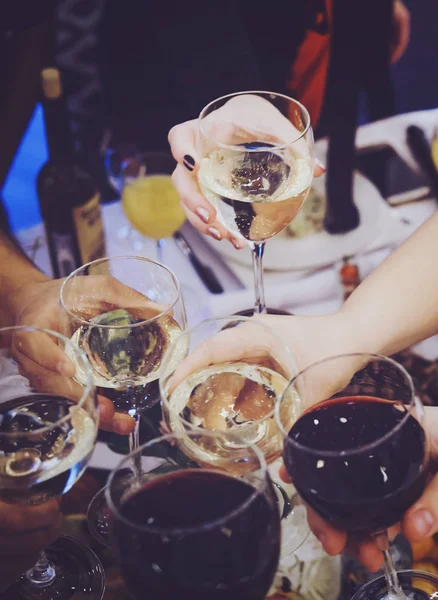Close up of people clinking glasses above the reastaurant table. Drinking toasts at a banquet. Celebration with drinks and food at a dinner party. Men and women feast an event. A drinking toast
