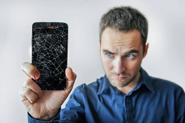 Грустный человек держит сломанный смартфон. Разбитый экран iphone . — стоковое фото