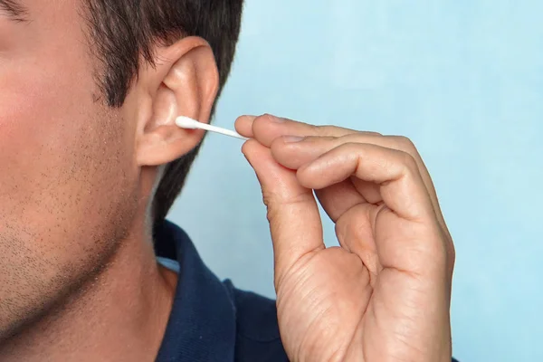 Image d'un bel homme debout sur un fond de mur bleu tenant un bourgeon de coton prendre soin de ses oreilles en le nettoyant — Photo