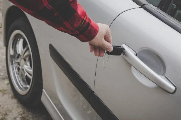 Primer plano de la mano de un hombre insertando una llave en la cerradura de la puerta de un coche. Hombre blanco irreconocible abre la puerta del vehículo con llave. Casualmente vestido hombre bloquea o desbloquea el automóvil. Brazo extendido — Foto de Stock