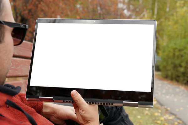 Close-up of casual dressed young man using modern digital tablet while sitting atpark, sun light. Blank white monitor screen. young guy lies in Park on a bench and watches a video on computer