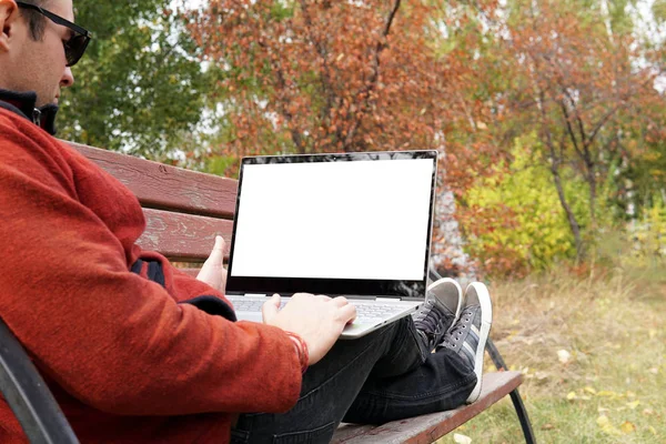 Fermer femme assise dans le parc à l'heure du coucher du soleil et à l'aide d'un ordinateur portable. Voyageur homme libre avec ultrabook sur le banc regardant l'écran du moniteur. Écran blanc pour la conception . — Photo