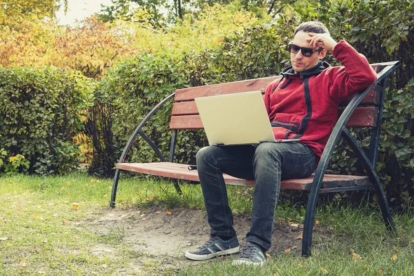 Jeune étudiant programmeur travailler étudier à l'extérieur. Développeur programmeur travaille avec son ordinateur portable dans le parc à l'extérieur du bureau. Homme pensif avec un ultrabook sur un banc — Photo