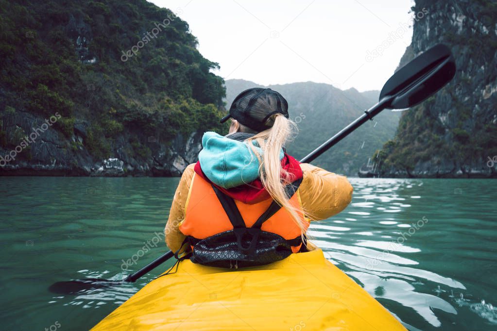 Girl kayaking on the seaside of Halong bay in Vietnam. Woman rowing oars in the boat. The view from the back