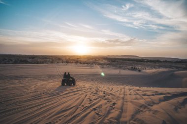 İki turist sabahın erken saatlerinde parlak bir güneş ile güzel bir şafak arka planda kum ulağı üzerinde dört bisiklet ebinmek. Mui ne. Vietnam Vietnam çölde Safari