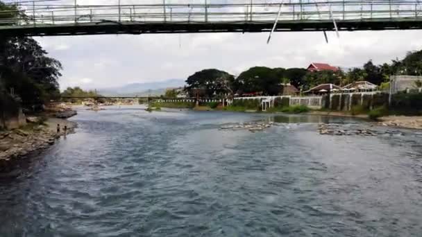 Vlucht van de drone is laag boven het wateroppervlak over de rivier onder de brug. — Stockvideo