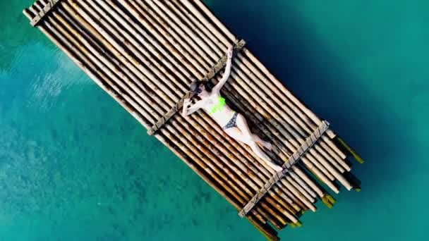 Jonge vrouw ligt op een houten vlot in een blauwe lagune en zonnebaden in de zon. Schoon water in de vijver. — Stockvideo