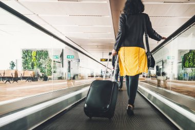 Seyahat bavulu ya da bavulu olan bir kadın yurt dışına seyahat için havaalanı terminali yolunda yürüyor. Konsept dünyayı dolaşma, turizm. Sarı etekli esmer yürüyen merdivene çıkıyor..