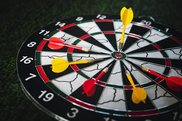 Winner yellow dart arrow hit center target of dartboard and other arrow loser metaphor marketing competition concept, on dark green background. Playing Darts