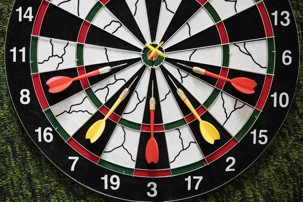 Winner yellow dart arrow hit center target of dartboard and other arrow loser metaphor marketing competition concept, on dark green background. Playing Darts