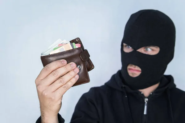 De Rover in de Balaclava telt het geld in de gestolen portefeuille. Dief in zwart masker Holding portemonnee en kijken naar camera. — Stockfoto