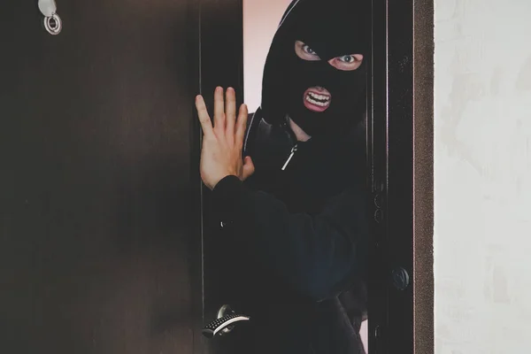 Evil gangster in een zwart masker bedekt zijn gezicht brak de deur en brak in de kamer en bedreigt de bewoners. begrip misdaad en geweld. banditry, gangster isme, racketeering, banditisme, — Stockfoto