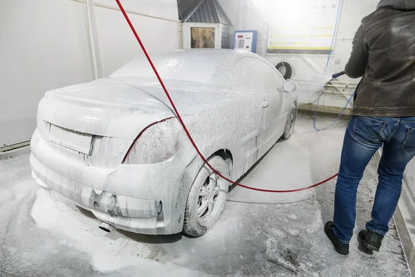 Hombre trabajador lavar el coche con lavadora de alta presión. Lavado de coches con espuma en la estación de lavado de coches. Un hombre rocía espuma en el coche de un spray especial . — Foto de Stock