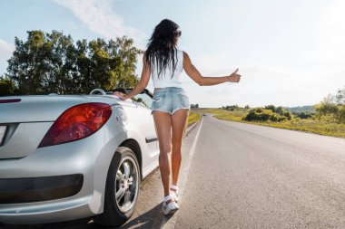 Yol sahnesi: seksi esmer kız onların kırık araba ve otostop yanında duran. Arka görüş. benzini bitti. Yolda araba ile ilgili sorunlar. Kırık araba. kız parmağını kaldırır. ülke yolu