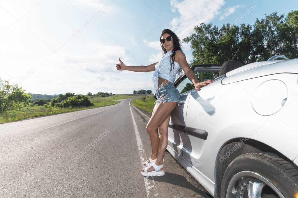 Road scene: sexy brunette girl standing near their broken car and hitchhiking. Rear view. ran out of gas. Problems with cars on the road. Broken car. girl raises her finger. country road