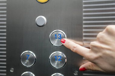 Woman in elevator or lift is pressing button to get into right floor only hand to be seen - close-up. 13 th floor clipart