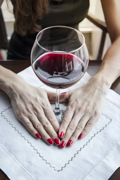 La mano de una mujer con un clavo rojo sostiene una copa con vino tinto, una gran copa de vino tinto en una servilleta blanca sobre la mesa en el restaurante . — Foto de Stock