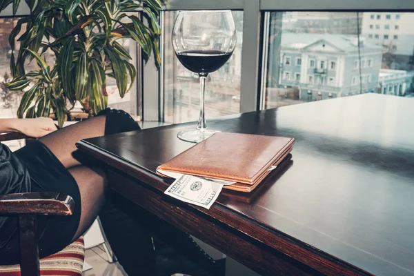 Propina generosa de cien dólares sobre la mesa en una carpeta de cuero. La chica se bebió el vino y pagó la cuenta. Una gran copa de vino sobre la mesa en un restaurante caro . — Foto de Stock