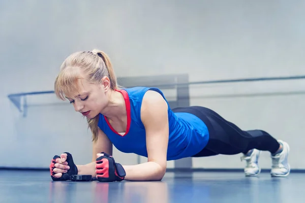 Mujer haciendo ejercicio push-up. Mujer fuerte haciendo entrenamiento crossfit. rubia se para en sus codos y mira el cronómetro en el suelo. ejercicio de resistencia — Foto de Stock