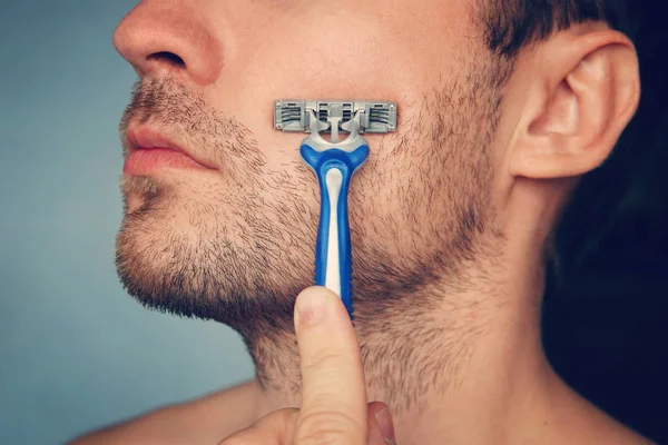 view of a young bearded man with a brutal razor. face on the blue background. big rough hairy bristles on the skin, side view close up