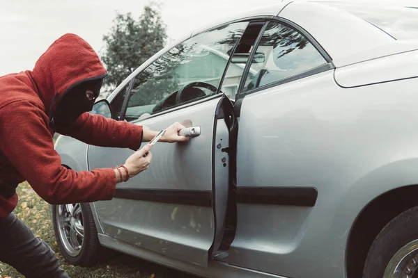 Auto dief in hoodie slaagde erin om de auto te ontgrendelen met behulp van de smartphone en auto link applicatie. Man met gemaskerde gezicht kreeg de toegang tot de cabine van het voertuig door mobiele app. crimineel ontgrendelt de auto. — Stockfoto