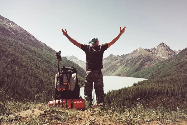 Standing sporty man with backpack on the mountain peak and beautiful mountains atbright sunny day. Landscape with man, rocks with snowy peaks, glacier, clouds in altay. Travel. Trekking. Vintage.