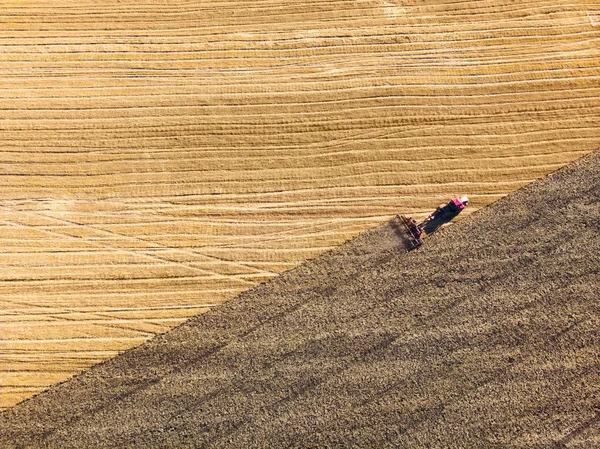 Z lotu ptaka dron pola żniw z ciągnikiem kosi suchą trawę. Jesienne żółte pole ze stogiem siana po żniwach widok z góry. Zbiory na polach. Zapasy siana na zimę. Widok z góry. — Zdjęcie stockowe