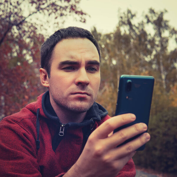 guy using smartphone device outdoor, outdoor portrait of young cheerful man texting an sms message at social networks, technology concept, displeasure, disaffection, resentment, frustration
