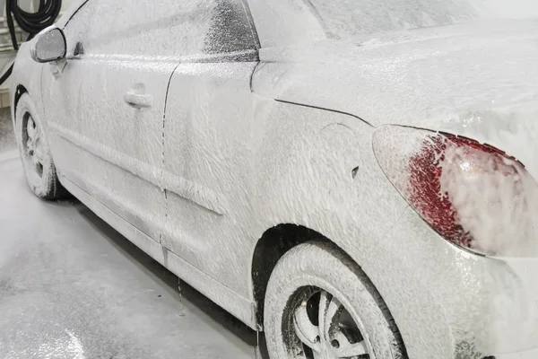 Coche está cubierto con espuma blanca en el lavado de coches en el garaje. Lavadora automática. Lavado automático de automóviles . — Foto de Stock