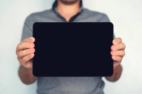 Young male holds a touch pad tablet on isolated white background. Large-size digital tablet with black screen is held by the man on the blurred backround. A touch pad in man\'s hands on the foreground