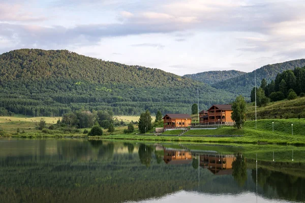 landscape of mountains and lakes with obecnym sky. Luxury expensive mansion made of wood in an ecologically clean mountain area is reflected in the water by the lake.