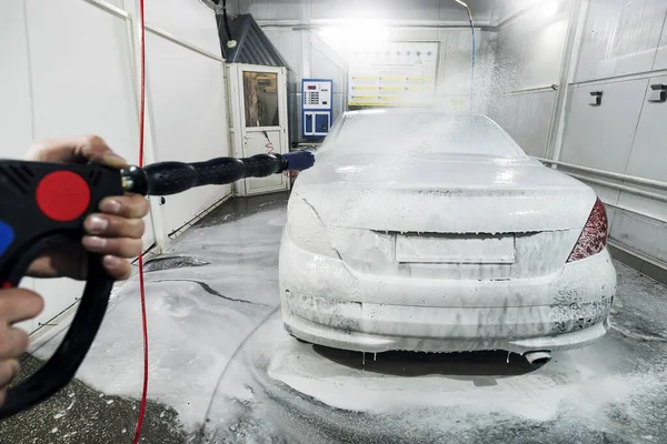 Un hombre rocía espuma en el coche de un spray especial. Lavado de coches con espuma en la estación de lavado de coches. Hombre trabajador lavar el coche con lavadora de alta presión — Foto de Stock