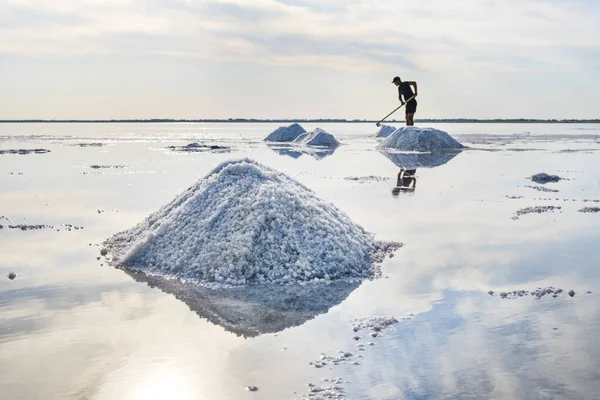 Molto sale si riflette nell'acqua. Un uomo con un rastrello produce sale. Bellissimo paesaggio con cielo blu — Foto Stock