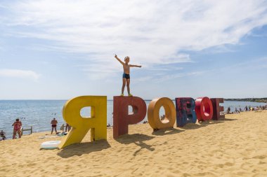 Göl ve turistlerin arka planındaki sarı kumun üzerinde Rusça yazılmış çok renkli Yarovoe yazıları. Altai bölgesindeki tatil köyünün Yarovoe adı. - Rusya. 7 Ağustos 2019